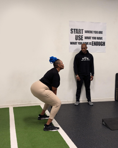 Gbenga coaching a member through a squat on the studio turf