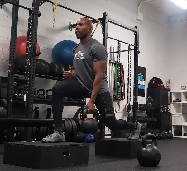 Gbenga coaching a split squat with kettlebells on the studio floor