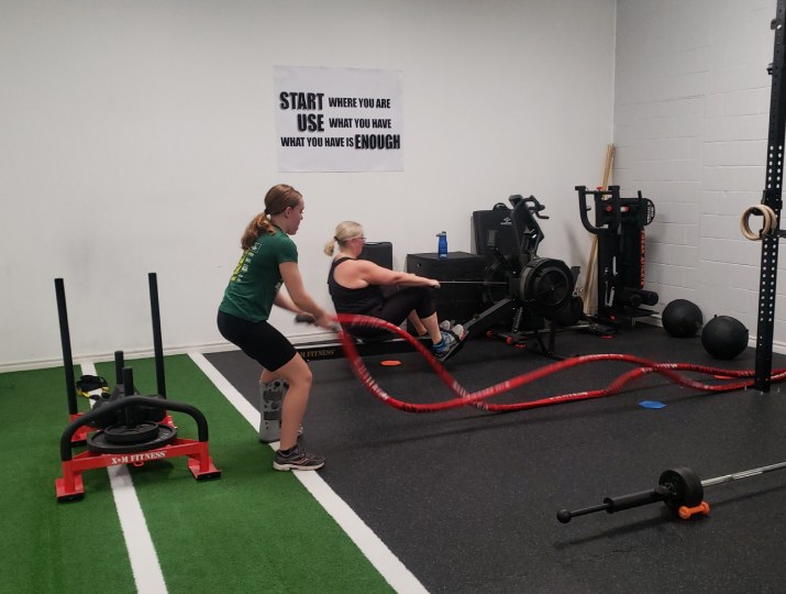 Two members working a sled and battle ropes on the studio turf